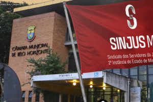 Montagem digital, à frente do edifício sede da Câmara Municipal de Belo Horizonte está flamulando ao vento uma bandeira do SINJUS.