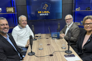 Imagem acessível: A imagem divulga o mais recente podcast do Se Liga, Minas. Na foto, mostra quatro pessoas em um estúdio, sentadas ao redor de uma mesa com microfones. Ao fundo, uma TV exibe o logotipo do podcast. O texto destaca: “Novo episódio do Se Liga, Minas traz debate sobre comunicação e o futuro do rádio”.
