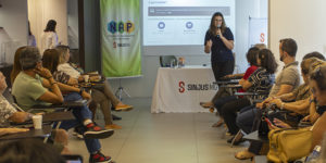 Imagem acessível: A imagem mostra aposentados e pensionistas reunidos em uma palestra promovida pelo NAP do SINJUS-MG, enquanto uma fisioterapeuta conduz a apresentação. O encontro teve como tema “Viver bem é uma questão de equilíbrio” e abordou a importância do equilíbrio físico, emocional e social para o bem-estar e a autonomia na terceira idade.