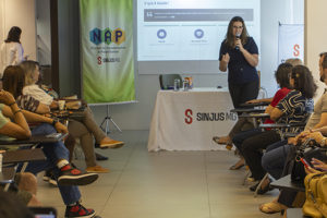 Imagem acessível: A imagem mostra aposentados e pensionistas reunidos em uma palestra promovida pelo NAP do SINJUS-MG, enquanto uma fisioterapeuta conduz a apresentação. O encontro teve como tema “Viver bem é uma questão de equilíbrio” e abordou a importância do equilíbrio físico, emocional e social para o bem-estar e a autonomia na terceira idade.