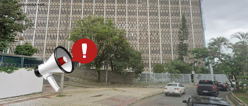 Foto diurna da fachada lateral do edifício situado à Praça Milton Campos, feita de baixo para cima. Sobre ela, é aplicada a figura de um megafone branco, vermelho e preto, do qual sai um balão vermelho com uma exclamação em branco, indicando atenção.