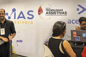 Montagem com duas fotos do estande da Vias Acessíveis na Mostra de Tecnologias Assistivas e Soluções de Acessibilidade. Na parte superior, uma mulher e um homem posam sorrindo atrás de uma bancada com materiais e equipamentos de acessibilidade, diante do painel da empresa. Na parte inferior, um expositor conversa com duas mulheres em frente a um notebook, enquanto apresenta soluções e recursos disponíveis no estande. Sobre as imagens, aparece a frase: “Inclusão efetiva de pessoas com deficiência exige acessibilidade desde a concepção dos eventos”. A Mostra reuniu empresas, universidades e empreendedores para apresentar tecnologias e soluções voltadas à acessibilidade e à inclusão.