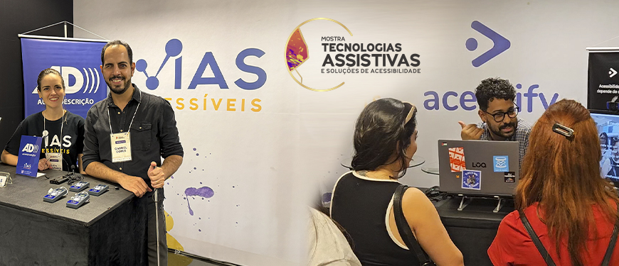 Montagem com duas fotos do estande da Vias Acessíveis na Mostra de Tecnologias Assistivas e Soluções de Acessibilidade. Na parte superior, uma mulher e um homem posam sorrindo atrás de uma bancada com materiais e equipamentos de acessibilidade, diante do painel da empresa. Na parte inferior, um expositor conversa com duas mulheres em frente a um notebook, enquanto apresenta soluções e recursos disponíveis no estande. Sobre as imagens, aparece a frase: “Inclusão efetiva de pessoas com deficiência exige acessibilidade desde a concepção dos eventos”. A Mostra reuniu empresas, universidades e empreendedores para apresentar tecnologias e soluções voltadas à acessibilidade e à inclusão.