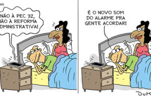 #ImagemAcessível: Charge com dois quadros. No primeiro, observa-se um casal na cama. Ao lado em cima de um móvel está um celular tocando o alarme com a seguinte frase: "NÃO À PEC 32. NÃO À REFORMA ADMINISTRATIVA". A mulher parece estranhar a situação. No segundo quadro, o homem explica: "É O NOVO SOM DO ALARME PRA GENTE ACORDAR".