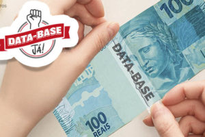 magem montagem, ao fundo branco se vê uma mão segurando uma nota rasgada no valor de cem reais na coloração azul, sendo colada por uma fita transparente contendo o escrito "DATA-BASE. Compondo a imagem se vê o logo campanha da data base já (sob um punho levantado se vê um selo com contorno vermelho e cinza, ao meio uma faixa na cor vermelho com o escrito Data-Base e abaixo a palavra já! .