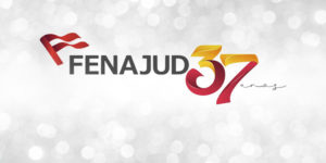 Imagem de celebração do aniversário da Fenajud, com fundo cinza claro em efeito desfocado, com pontos de luz que lembram brilho. No centro, está o logotipo da Fenajud, com um símbolo de bandeira vermelha à esquerda e a palavra “FENAJUD” em letras maiúsculas escuras. Ao lado, em destaque, aparece o número “37” em grande tamanho, com um degradê em tons de amarelo, laranja e vermelho, seguido da palavra “anos” em estilo manuscrito.