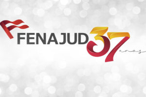 Imagem de celebração do aniversário da Fenajud, com fundo cinza claro em efeito desfocado, com pontos de luz que lembram brilho. No centro, está o logotipo da Fenajud, com um símbolo de bandeira vermelha à esquerda e a palavra “FENAJUD” em letras maiúsculas escuras. Ao lado, em destaque, aparece o número “37” em grande tamanho, com um degradê em tons de amarelo, laranja e vermelho, seguido da palavra “anos” em estilo manuscrito.