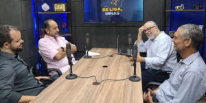 Num cenário em tons de azul há uma mesa com microfones onde estão 4 pessoas: o anfitrião do podcast Se liga Minas, Orion Teixeira; o ex-prefeito de Belo Horizonte, Alexandre Kalil; e os dirigentes do SINJUS-MG, Felipe Rodrigues (diretor de Assuntos Jurídicos) e Alex Aguiar (diretor de Finanças).