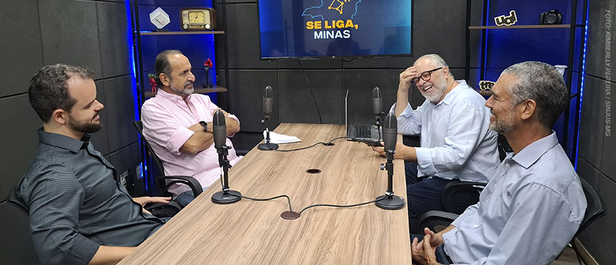 Num cenário em tons de azul há uma mesa com microfones onde estão 4 pessoas: o anfitrião do podcast Se liga Minas, Orion Teixeira; o ex-prefeito de Belo Horizonte, Alexandre Kalil; e os dirigentes do SINJUS-MG, Felipe Rodrigues (diretor de Assuntos Jurídicos) e Alex Aguiar (diretor de Finanças).