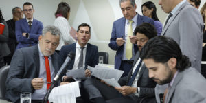 A imagem mostra um grupo de parlamentares reunidos em uma sala da ALMG, discutindo e analisando documentos. O ambiente é formal, com todos trajando ternos. O texto sobre a imagem informa que o Propag começou a tramitar na ALMG e que o SINJUS está intensificando articulações políticas em várias esferas, reforçando sua atuação na defesa dos direitos das servidoras e servidores mineiros