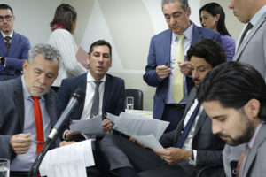 A imagem mostra um grupo de parlamentares reunidos em uma sala da ALMG, discutindo e analisando documentos. O ambiente é formal, com todos trajando ternos. O texto sobre a imagem informa que o Propag começou a tramitar na ALMG e que o SINJUS está intensificando articulações políticas em várias esferas, reforçando sua atuação na defesa dos direitos das servidoras e servidores mineiros