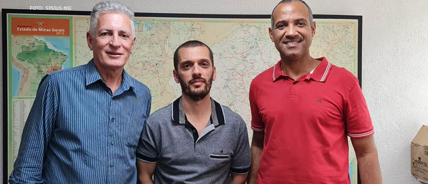 Há 3 homens lado a lado. Do lado esquerdo está um homem branco de cabelos brancos, trajando camisa azul e calça cinza (Deputado Federal Rogério Correia), ao centro está um homem branco de cabelos castanhos bem curtos, ele usa uma camisa cinza e uma calça jeans (Alexandre Pires, Coordenador - geral do SINJUS); à direita está um homem negro, de cabelos grisalhos bem curtos, ele usa uma camisa vermelha e uma calça jeans preta (Wagner Ferreira - diretor de assuntos Jurídico do SINJUS e vereador de Belo Horizonte).