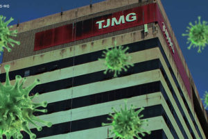 Fachada da sede do Tribunal de Justiça de Minas Gerais, na Avenida Afonso Pena em Belo Horizonte. No topo do edifício há um letreiro com fundo vermelho e a sigla TJMG em branco. Sobre a imagem do edifício sede, foram aplicados modelos 3D do coronavírus, patógeno causador da Covid-19.