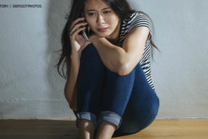 Imagem Acessível: Mulher sentada no chão com postura e expressão facial de medo, ela está falando ao telefone.