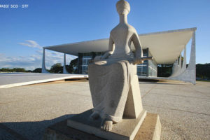 Fachada da sede do STF, em Brasília, em destaque está a escultura que representa a deusa grega da Justiça, Themis. Ela está sentada com olhos vendados e tem uma espada em seu colo.
