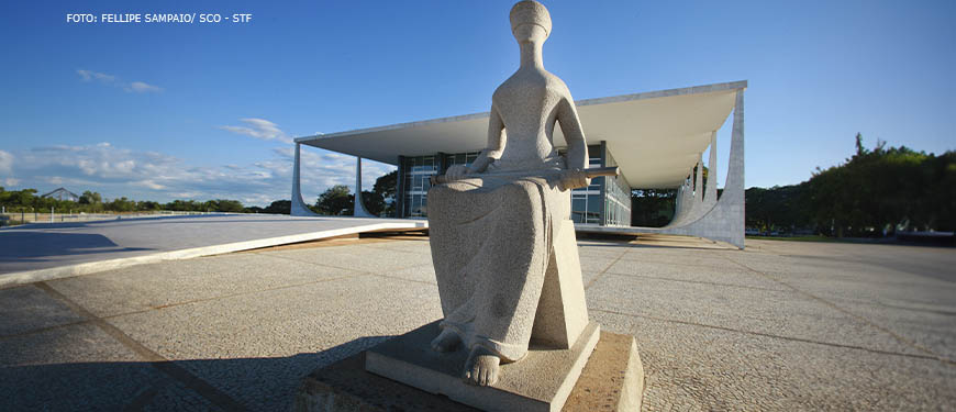 Fachada da sede do STF, em Brasília, em destaque está a escultura que representa a deusa grega da Justiça, Themis. Ela está sentada com olhos vendados e tem uma espada em seu colo.