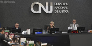 Mesa diretiva do CNJ (Conselho Nacional de Justiça), ao centro está a presidente do CNJ, Ministra Rosa Weber, ela é uma mulher de pele branca, tem cabelos loiros, lisos e curtos; ela veste um traje social escuro estampado e usa óculos de grau.