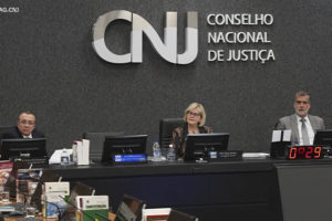 Mesa diretiva do CNJ (Conselho Nacional de Justiça), ao centro está a presidente do CNJ, Ministra Rosa Weber, ela é uma mulher de pele branca, tem cabelos loiros, lisos e curtos; ela veste um traje social escuro estampado e usa óculos de grau.