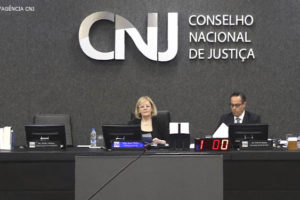 Imagem Acessível: Ministra Rosa Weber em reunião com conselheiros do Conselho Nacional da Justiça, em destaque está o letreiro inox do CNJ.