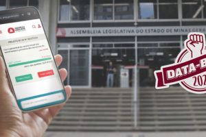 A imagem mostra uma campanha de mobilização para que as pessoas votem a favor do Projeto de Lei da Data-Base 2024, disponível no site da ALMG. Em destaque, há uma mão segurando um celular com a tela aberta na página do projeto de lei no site da ALMG, onde é possível clicar nos botões “Votar a favor” ou “Votar contra”. Ao fundo, aparece a fachada da Assembleia Legislativa. Um selo com um punho erguido e os dizeres “DATA-BASE 2024” reforça o tom de luta e reivindicação.