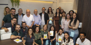 Imagem acessível: A imagem mostra um grupo de pessoas reunido durante a inauguração do Espaço Terapêutico Nicolau Prímola, na sede do SINJUS-MG. Em destaque, o título diz “SINJUS inaugura Espaço Nicolau Prímola para ampliar ações de saúde e acolhimento”. Na base da imagem, aparece a logomarca do SINJUS.