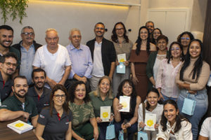 Imagem acessível: A imagem mostra um grupo de pessoas reunido durante a inauguração do Espaço Terapêutico Nicolau Prímola, na sede do SINJUS-MG. Em destaque, o título diz “SINJUS inaugura Espaço Nicolau Prímola para ampliar ações de saúde e acolhimento”. Na base da imagem, aparece a logomarca do SINJUS.