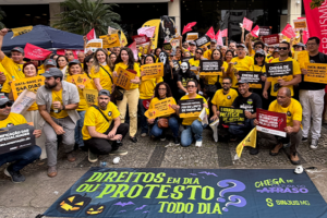 Manifestação de servidores em frente à sede do TJMG. O grupo, majoritariamente vestido de amarelo, segura cartazes cobrando direitos como Data-Base, Promoção Vertical e combate à terceirização. Algumas pessoas usam máscaras de terror em referência ao Halloween. Em primeiro plano, uma grande faixa no chão traz a frase “Direitos em dia ou protesto todo dia”, acompanhada de abóboras, morcegos e elementos de Halloween.