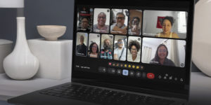 A imagem mostra uma tela de notebook exibindo uma reunião virtual com várias pessoas sorrindo, representando integrantes do Coletivo de Negras e Negros da Fenajud.