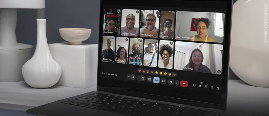 A imagem mostra uma tela de notebook exibindo uma reunião virtual com várias pessoas sorrindo, representando integrantes do Coletivo de Negras e Negros da Fenajud.