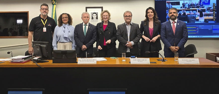 Na mesa principal de uma audiência no Congresso Nacional, está o coordenador-geral da Fenajud, junto de parlamentares e outros participantes do debate.