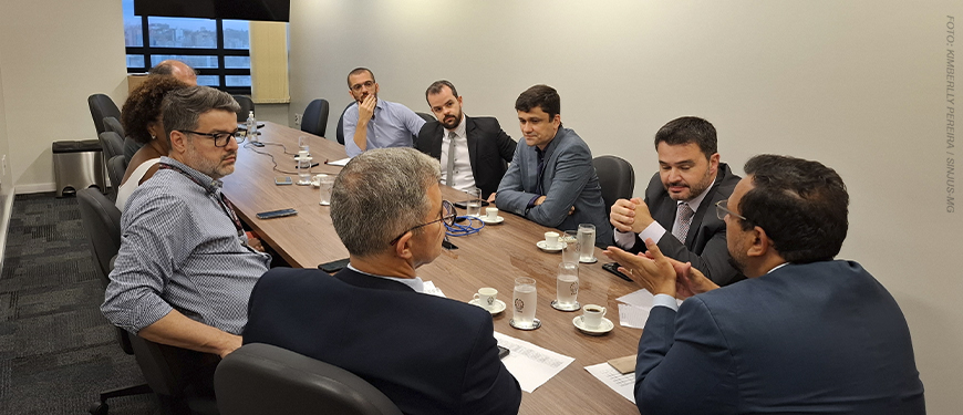 Imagem Acessível: A imagem mostra uma reunião formal entre representantes do SINJUS-MG e do TJMG, realizada em uma sala de reuniões com mesa retangular. O texto em destaque informa: “SINJUS conquista reajuste substancial do Auxílio-Saúde”, simbolizando uma vitória importante para os servidores do Judiciário mineiro, resultado da atuação sindical constante e articulada junto ao Tribunal. No inferior da imagem, é visível o logotipo do SINJUS-MG.