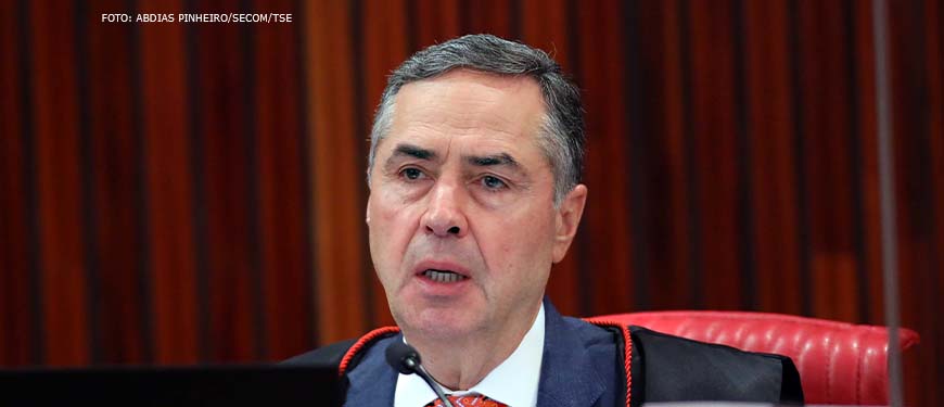 Foto do ministro do Supremo Tribunal Federal Luís Roberto Barroso (homem de pele clara, cabelos grisalhos e utilizando terno e toga).