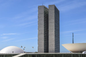 Imagem Acessível: A imagem mostra ao fundo o céu azul e a arquitetura icônica do Congresso, com as torres e cúpulas brancas. Em destaque, o texto: “Alerta: Câmara retoma debate sobre Reforma Administrativa e PEC 66 nesta 6ªf.”. A imagem sinaliza urgência para os servidores públicos.