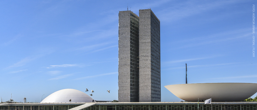 Imagem Acessível: A imagem mostra ao fundo o céu azul e a arquitetura icônica do Congresso, com as torres e cúpulas brancas. Em destaque, o texto: “Alerta: Câmara retoma debate sobre Reforma Administrativa e PEC 66 nesta 6ªf.”. A imagem sinaliza urgência para os servidores públicos.
