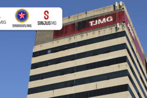 Edifício-sede do Tribunal de Justiça de Minas Gerais, a edificação tem pilares em concreto, janelas em vidro escuro que formam linhas horizontais e uma placa vermelha com o letreiro TJMG. sobre essa foto, há a aplicação digital dos logos dos três sindicatos que representam os servidores da Justiça, o Sindojus-MG, o Serjusmig e o SINJUS-MG.