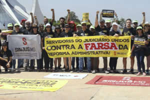 Grupo de manifestantes do SINJUS-MG posa em frente à Catedral de Brasília, durante ato nacional contra a Reforma Administrativa. As pessoas vestem camisetas pretas e seguram faixas com mensagens como “Servidores do Judiciário unidos contra a farsa da Reforma Administrativa” e bandeiras com o logotipo do Sindicato.