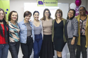 Integrantes do Núcleo das Mulheres posam abraçadas uma do lado da outra juntamente com as coordenadoras do NM Adriana Teodoro e Janaína Barbosa.