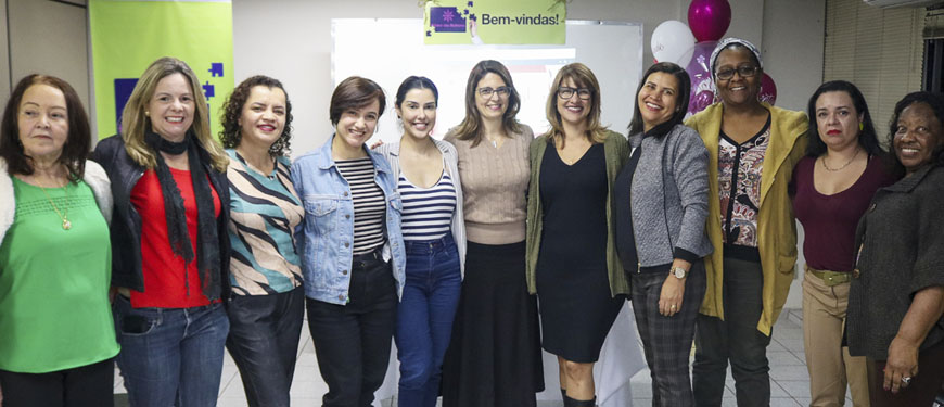 Integrantes do Núcleo das Mulheres posam abraçadas uma do lado da outra juntamente com as coordenadoras do NM Adriana Teodoro e Janaína Barbosa.