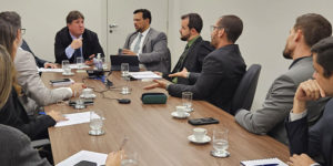 Registro de uma reunião em uma sala de reuniões do Tribunal de Justiça de Minas Gerais. Dirigentes dos sindicatos estão ao sentados ao redor de uma mesa, todos em trajes formais, envolvidos em uma conversa séria. No centro da imagem, está o juiz auxiliar Thiago Colnado, junto do coordenador-geral e do diretor de Assuntos Jurídicos do SINJUS, Alexandre Pires e Felipe Rodrigues, eles gesticulam energicamente enquanto falam. O clima aparenta ser de discussão ou negociação.