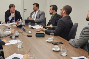 Registro de uma reunião em uma sala de reuniões do Tribunal de Justiça de Minas Gerais. Dirigentes dos sindicatos estão ao sentados ao redor de uma mesa, todos em trajes formais, envolvidos em uma conversa séria. No centro da imagem, está o juiz auxiliar Thiago Colnado, junto do coordenador-geral e do diretor de Assuntos Jurídicos do SINJUS, Alexandre Pires e Felipe Rodrigues, eles gesticulam energicamente enquanto falam. O clima aparenta ser de discussão ou negociação.