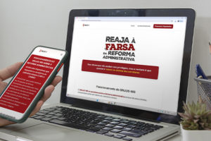 A imagem possui o fundo em tons de cinza mostrando uma pessoa segurando um celular diante de um notebook. Ambos exibem o hotsite do SINJUS sobre a Reforma Administrativa, com o título “Reaja à Farsa da Reforma Administrativa”.