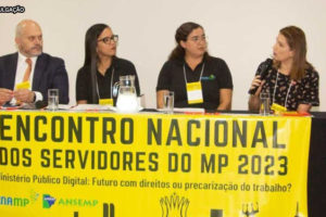 Grupo de seis pessoas, sendo elas três homens e três mulheres em uma mesa com um banner amarelo com os escritos Encontro Nacional dos Servidores do MP 2023
