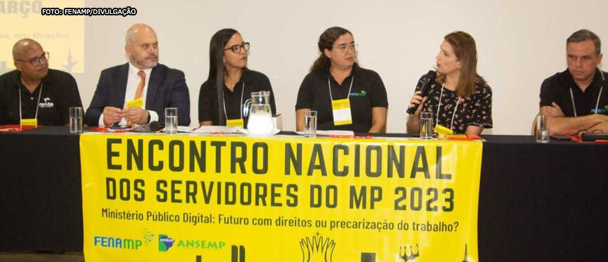 Grupo de seis pessoas, sendo elas três homens e três mulheres em uma mesa com um banner amarelo com os escritos Encontro Nacional dos Servidores do MP 2023