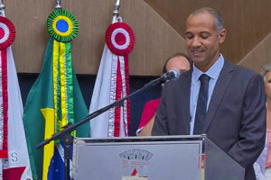 Wagner Ferreira fala no púlpito do Plenário da Câmara Municipal de Belo Horizonte, ele é um homem negro, com cabelos grisalhos bem curtos, um pouco calvo, ele usa um traje social cinza com uma camisa e gravata azuis.