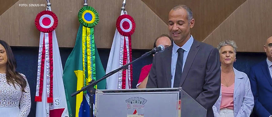 Wagner Ferreira fala no púlpito do Plenário da Câmara Municipal de Belo Horizonte, ele é um homem negro, com cabelos grisalhos bem curtos, um pouco calvo, ele usa um traje social cinza com uma camisa e gravata azuis.
