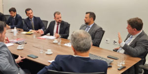 A imagem mostra uma reunião institucional, com homens de terno sentados ao redor de uma mesa. Entre os participantes estão representantes da presidência do Tribunal de Justiça de Minas Gerais, o coordenador-geral do SINJUS-MG, Felipe Rodrigues, e o diretor administrativo do Sindicato, Alexandre Pires. O sindicalista Felipe Rodrigues gesticula energicamente, enquanto dirige o olhar para o juiz auxiliar Thiago Colnago.