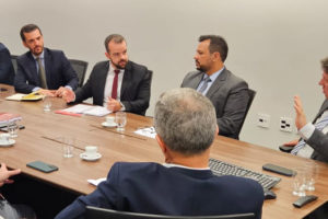 A imagem mostra uma reunião institucional, com homens de terno sentados ao redor de uma mesa. Entre os participantes estão representantes da presidência do Tribunal de Justiça de Minas Gerais, o coordenador-geral do SINJUS-MG, Felipe Rodrigues, e o diretor administrativo do Sindicato, Alexandre Pires. O sindicalista Felipe Rodrigues gesticula energicamente, enquanto dirige o olhar para o juiz auxiliar Thiago Colnago.