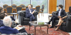 A imagem mostra um grupo de magistrados e autoridades reunidos em uma sala ampla e elegante, com poltronas de couro, mesa de centro e tapete vermelho. Ao fundo, grandes janelas revelam uma paisagem verde.