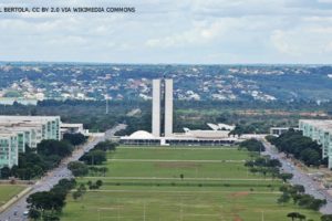 #ImagemAcessível: Imagem aérea de Brasília onde se vê o Congresso Nacional no centro da imagem e os ministérios de cada lado.