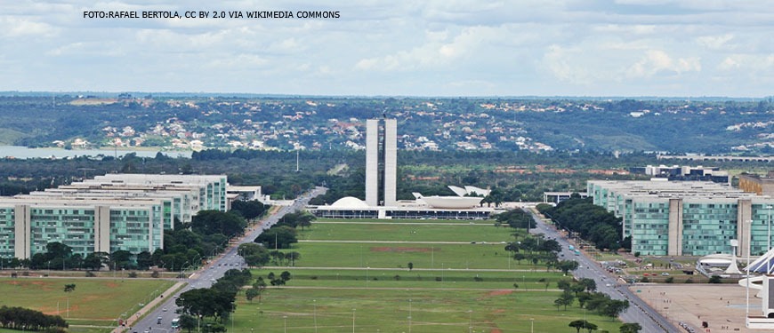#ImagemAcessível: Imagem aérea de Brasília onde se vê o Congresso Nacional no centro da imagem e os ministérios de cada lado.
